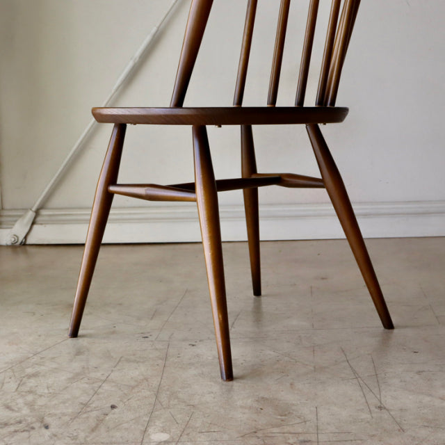 Mid-century British ERCOL Quaker chair in teak with slender spindle back, tapered legs, and visible wood grain.