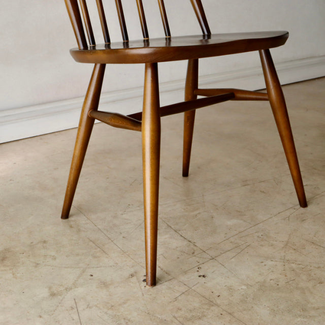 Mid-century British Ercol Quaker chair in warm teak with visible wood grain, slender spindle back and tapered legs.