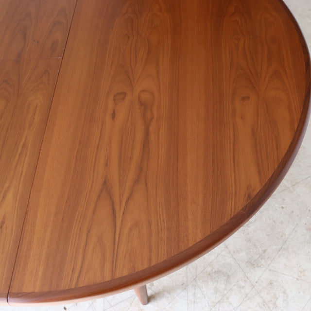 Round vintage teak dining table by British brand G-Plan with smooth wood grain and slender mid-century legs, inspired by.