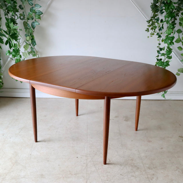 Mid-century British G-Plan vintage teak dining table with oval top and tapered round legs, smooth wood grain visible.
