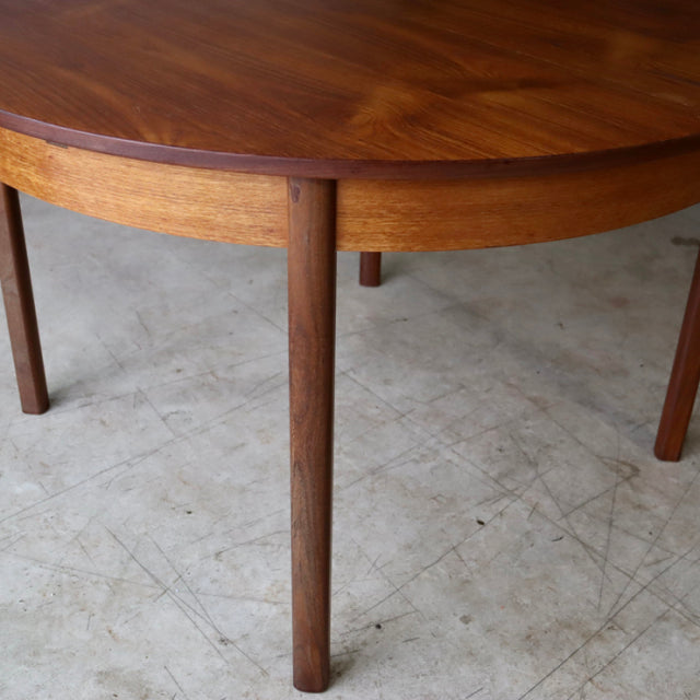 Vintage mid-century British teak dining table with round top, smooth wood grain, and slender cylindrical legs.