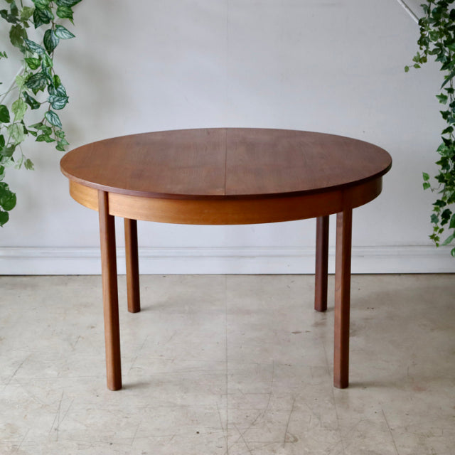 Vintage mid-century teak dining table with round top and straight cylindrical legs, British-Denmark design, smooth wood.