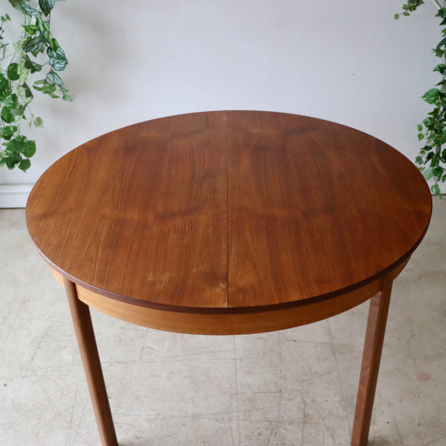 Vintage mid-century round teak dining table from Denmark with smooth wood grain and slender tapered legs.