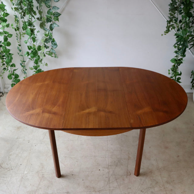 Vintage teak dining table with oval top showcasing rich wood grain, slender mid-century British legs, Danish design.