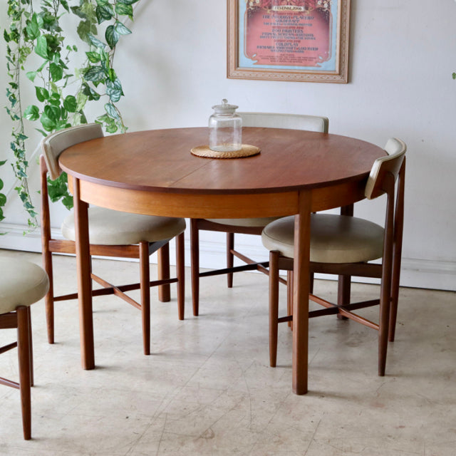 Round vintage teak dining table with smooth wood grain and slender mid-century British-style legs, paired with beige.