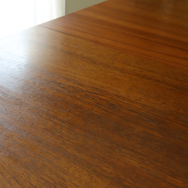 Vintage teak dining table with rich wood grain, mid-century British-Denmark design, smooth rectangular surface.