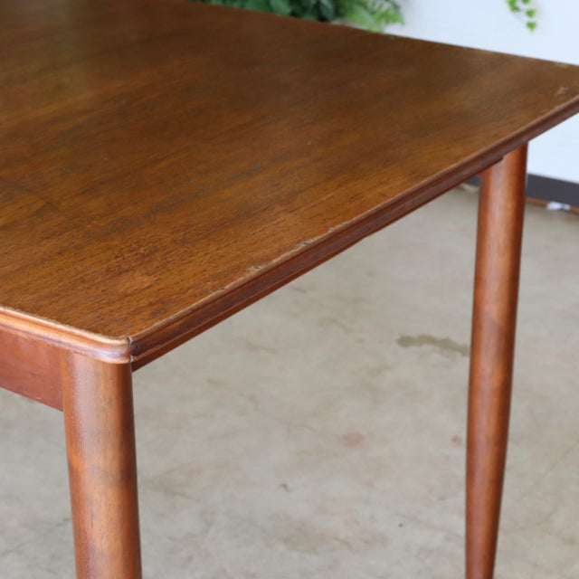 Vintage mid-century teak dining table with smooth wood grain, slender rounded legs, and a warm British-Danish design.