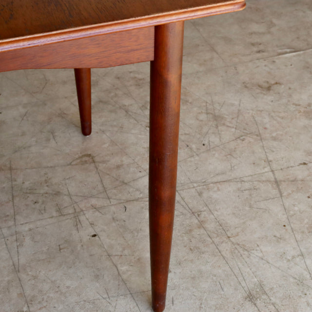 Mid-century British vintage teak dining table corner with tapered round legs and rich wood grain finish on concrete floor.