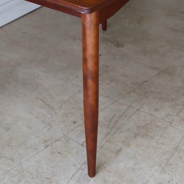 Mid-century vintage teak dining table corner with tapered rounded leg and smooth wood grain, British-Denmark style.