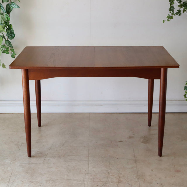 Vintage teak mid-century dining table with rectangular top, tapered legs, smooth wood grain from British-Denmark style.