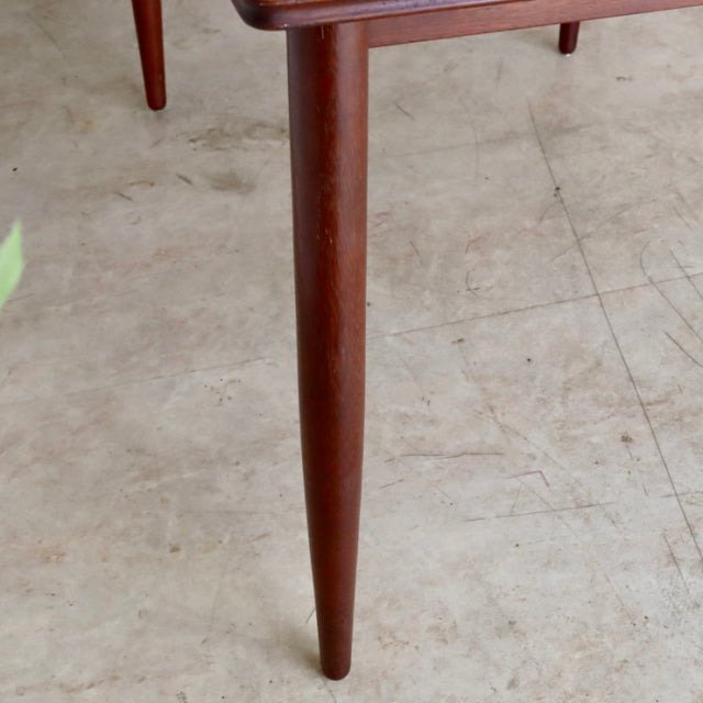 Mid-century British teak dining table leg with smooth wood grain and tapered rounded profile on stone floor.