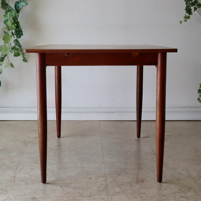 Vintage mid-century teak dining table with rich wood grain, slender tapered legs, and British-Denmark design influence.