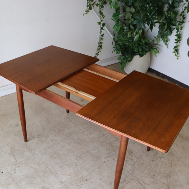 Mid-century British vintage teak dining table with extendable top and tapered legs, rich wood grain visible, classic.