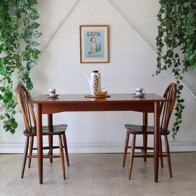 Vintage teak dining table with smooth grain, mid-century British design, paired with curved-back wooden chairs, styled in a.