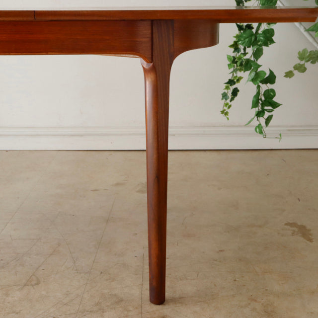 Mid-century British vintage teak dining table leg with smooth wood grain and tapered design under oval top.