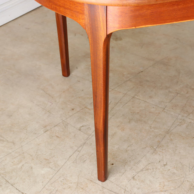 Mid-century British teak dining table with oval top, smooth rounded edges, and tapered legs showing rich wood grain.
