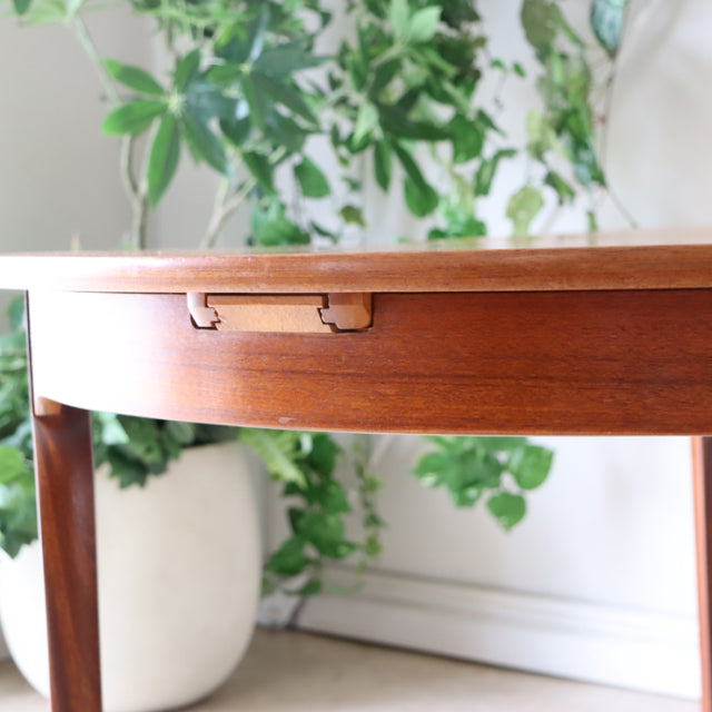 Mid-century British vintage teak oval dining table with smooth wood grain and tapered legs in a bright room.