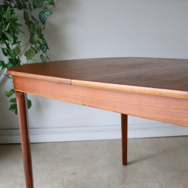 Oval vintage teak dining table by NATHAN with mid-century British design, smooth wood grain, and slender tapered legs.