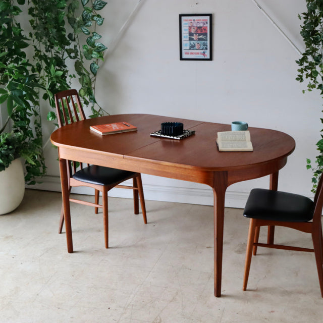 Oval vintage teak dining table with smooth rounded edges, slender tapered legs, and visible wood grain in a mid-century.