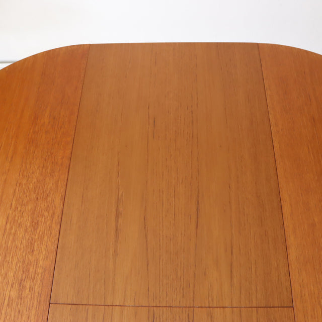 Close-up of vintage British mid-century teak dining table top with smooth wood grain and rounded edges.