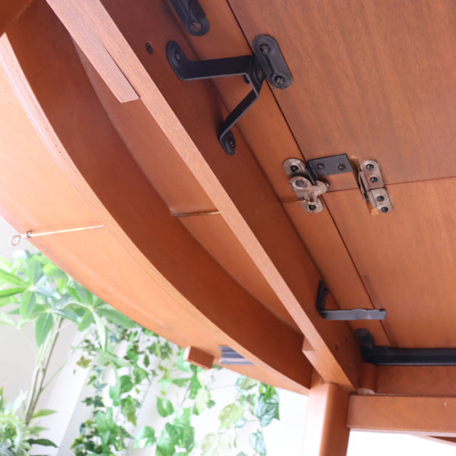 Mid-century British teak dining table by Greaves and Thomas showing rich wood grain, metal hinge, and sturdy underside frame .