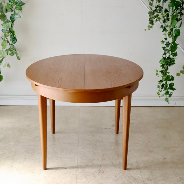 Vintage British mid-century teak dining table by GREAVESandTHOMAS with round top and slender tapered legs.