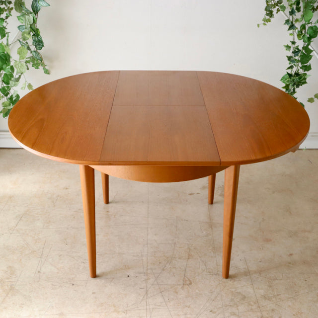Vintage teak oval dining table with rich wood grain, slender tapered legs, mid-century British-Denmark design by.