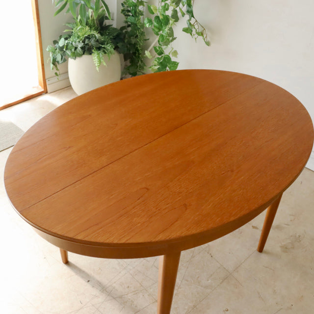 Vintage British mid-century teak dining table with smooth oval top and tapered legs, showcasing fine wood grain and Danish.