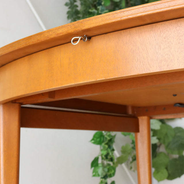 Mid-century British teak dining table by GREAVESandTHOMAS with smooth oval top, visible wood grain, and slender rounded legs.