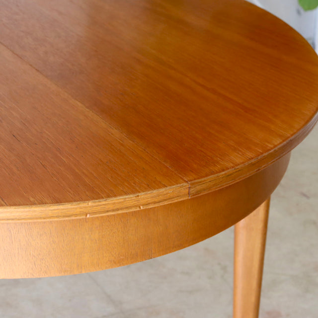 Vintage teak mid-century round dining table by Greaves and Thomas with smooth wood grain and tapered legs.