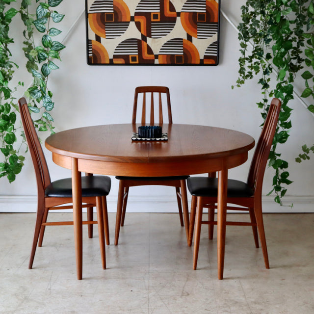 Vintage teak G-Plan round dining table with tapered legs, showcasing rich wood grain and mid-century British design, flanked .