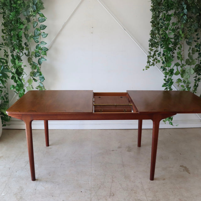 Mid-century British McIntosh teak dining table with rich wood grain, extending top, and slender tapered legs.