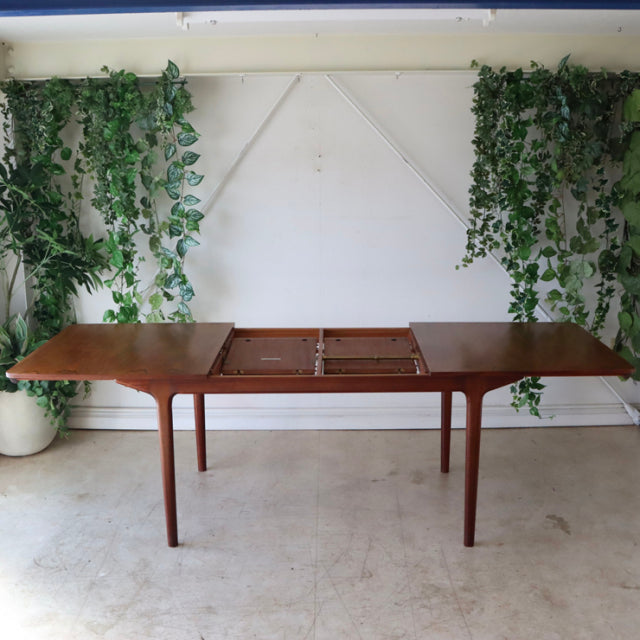Vintage mid-century McIntosh teak dining table with warm wood grain, tapered legs, and extendable center, British-Denmark.