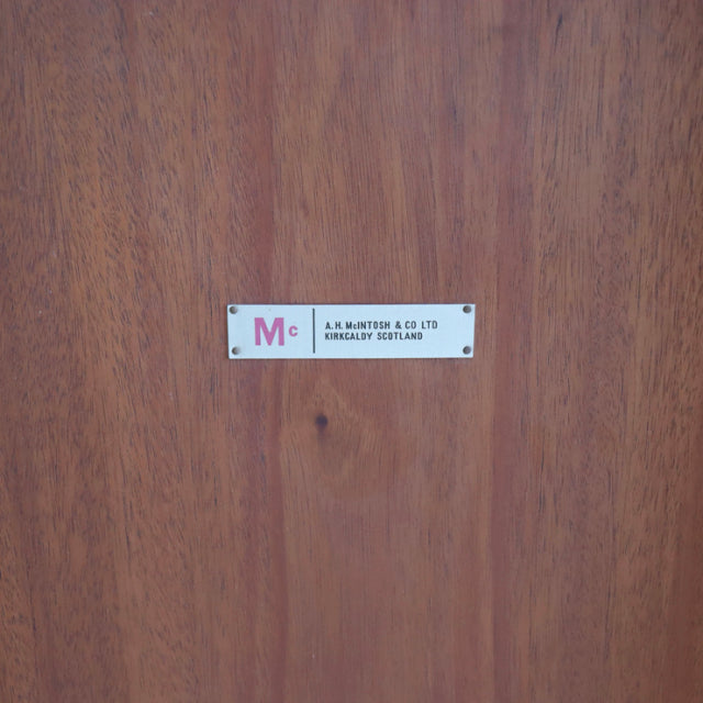 Close-up of vintage mid-century British McIntosh dining table showcasing smooth teak wood grain and metal brand label inset.