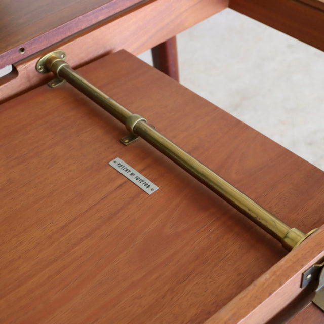 Vintage McIntosh teak dining table underside showing brass support bar and rich wood grain, mid-century British design with.