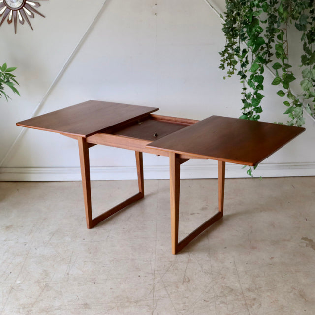 Mid-century British teak dining table with extendable leaves, rectangular top, and straight legs showing rich wood grain.