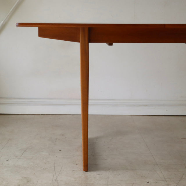 Mid-century British vintage teak dining table with tapered legs and smooth rectangular top showing rich wood grain.
