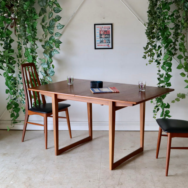 Mid-century British teak dining table with rectangular top, clean lines, and sturdy angular legs surrounded by two matching.