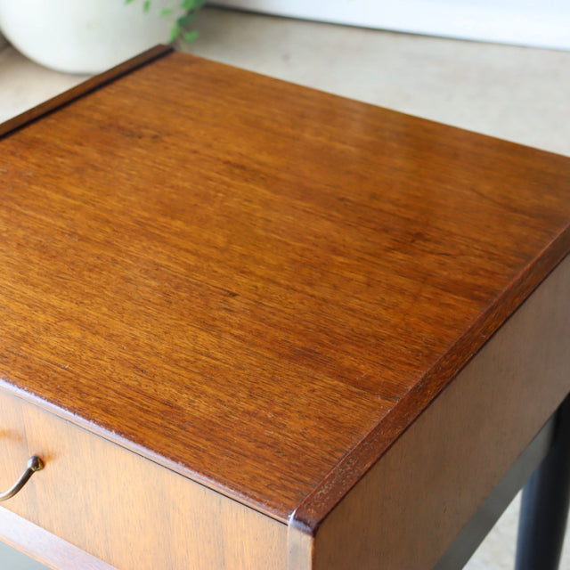 Vintage British mid-century teak bedside cabinet top with rich wood grain and black tapered legs.