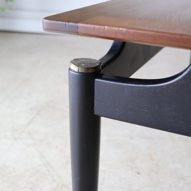 Mid-century British G-Plan teak and black wood coffee table corner with rounded leg and brass-capped detail.