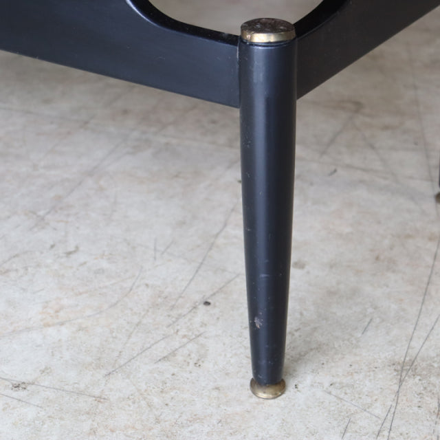 Close-up of black tapered mid-century teak coffee table leg with brass cap and foot, vintage British G-plan style.