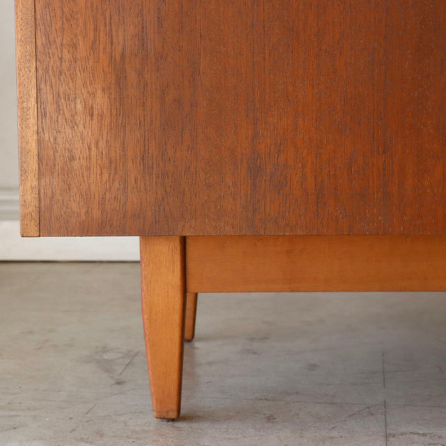 Close-up of vintage teak wood cabinet corner showing rich grain and tapered mid-century British Denmark-style leg.