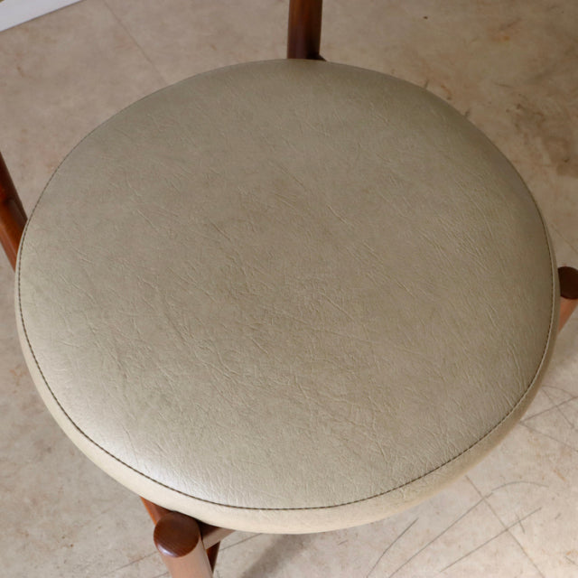 Round beige leather seat cushion with subtle grain texture on vintage teak mid-century British dining chair legs visible.