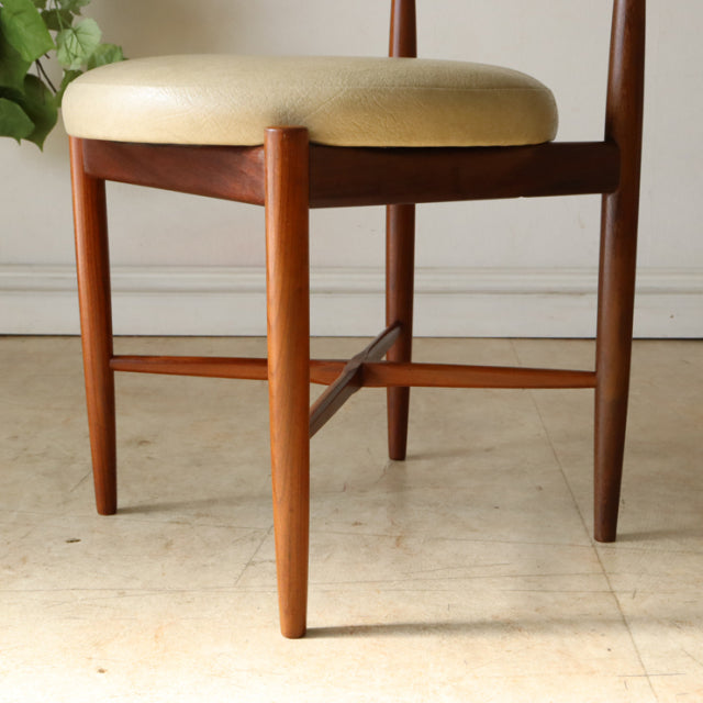 Set of four vintage British G-Plan mid-century teak dining chairs with rounded beige upholstered seats and tapered legs.