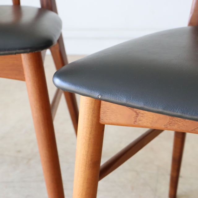 Set of four vintage teak dining chairs from mid-century Denmark with British design influence, featuring black leather seats .