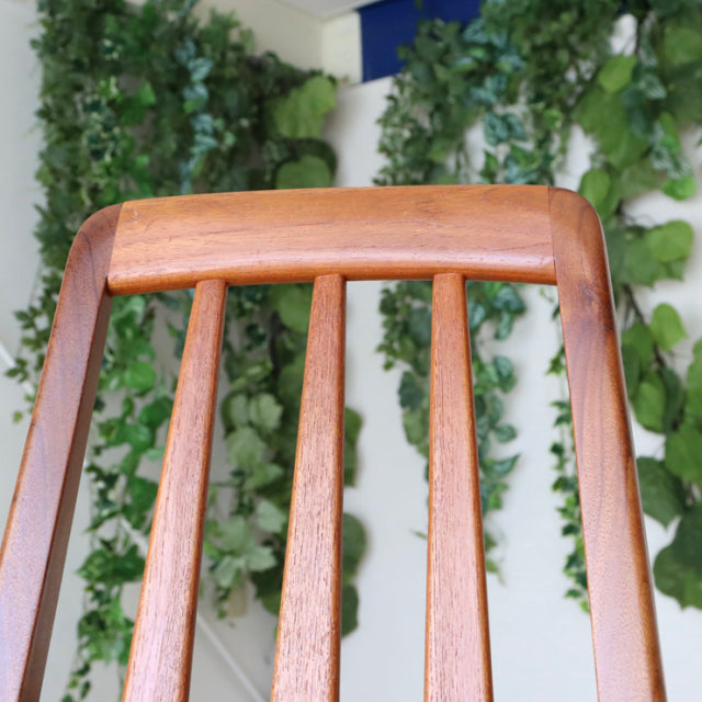 Set of four vintage mid-century Danish teak dining chairs with clean lines and vertical slat backs against a green leafy.
