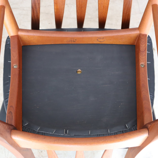Vintage teak dining chair seat showing smooth wood grain frame and black upholstered cushion with brass center detail,.
