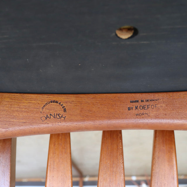 Close-up of mid-century vintage teak dining chair backrest showing curved wood grain, Danish craftsmanship stamp, and.