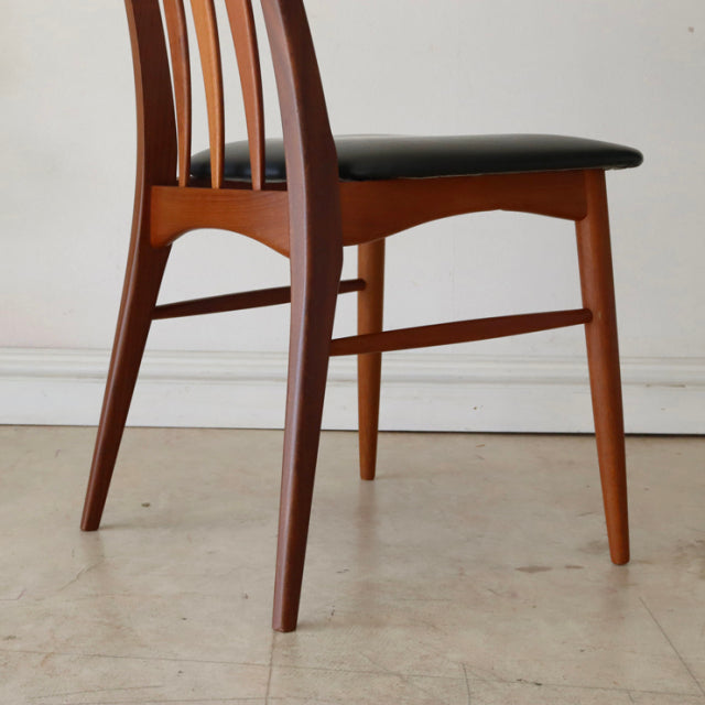 Mid-century vintage Danish teak dining chair with curved slatted back and black leather seat, showcasing sleek tapered legs.