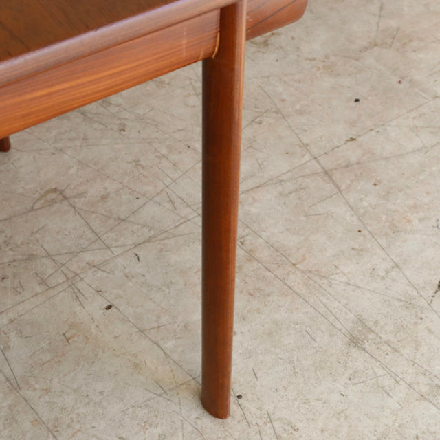 Mid-century British teak dining table leg with smooth wood grain and rounded square frame detail on concrete floor.